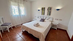 Un dormitorio ordenado con una cama, una silla y dos lámparas fijadas a la pared.
