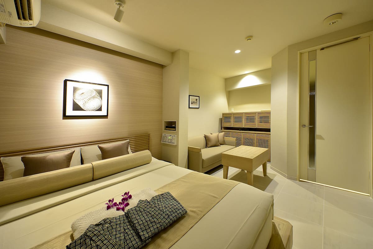 A hotel room with a bed, a sofa, a small table, and a bathroom.