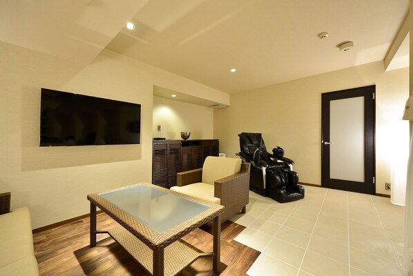 A living room with a glass-top table, wicker furniture, a flat-screen TV, and a door.