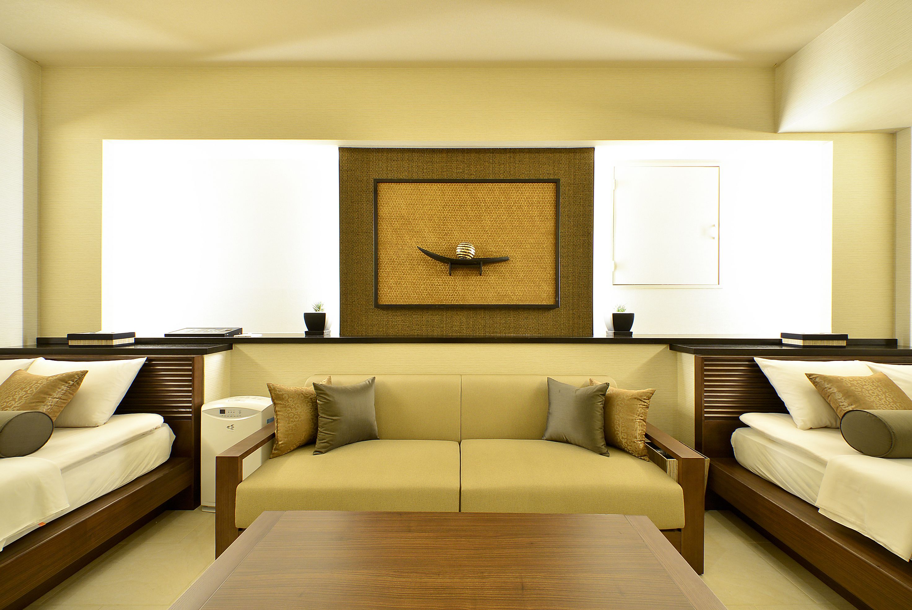 A modern hotel room with a sofa bed, a wooden coffee table, and a wall-mounted decorative piece.