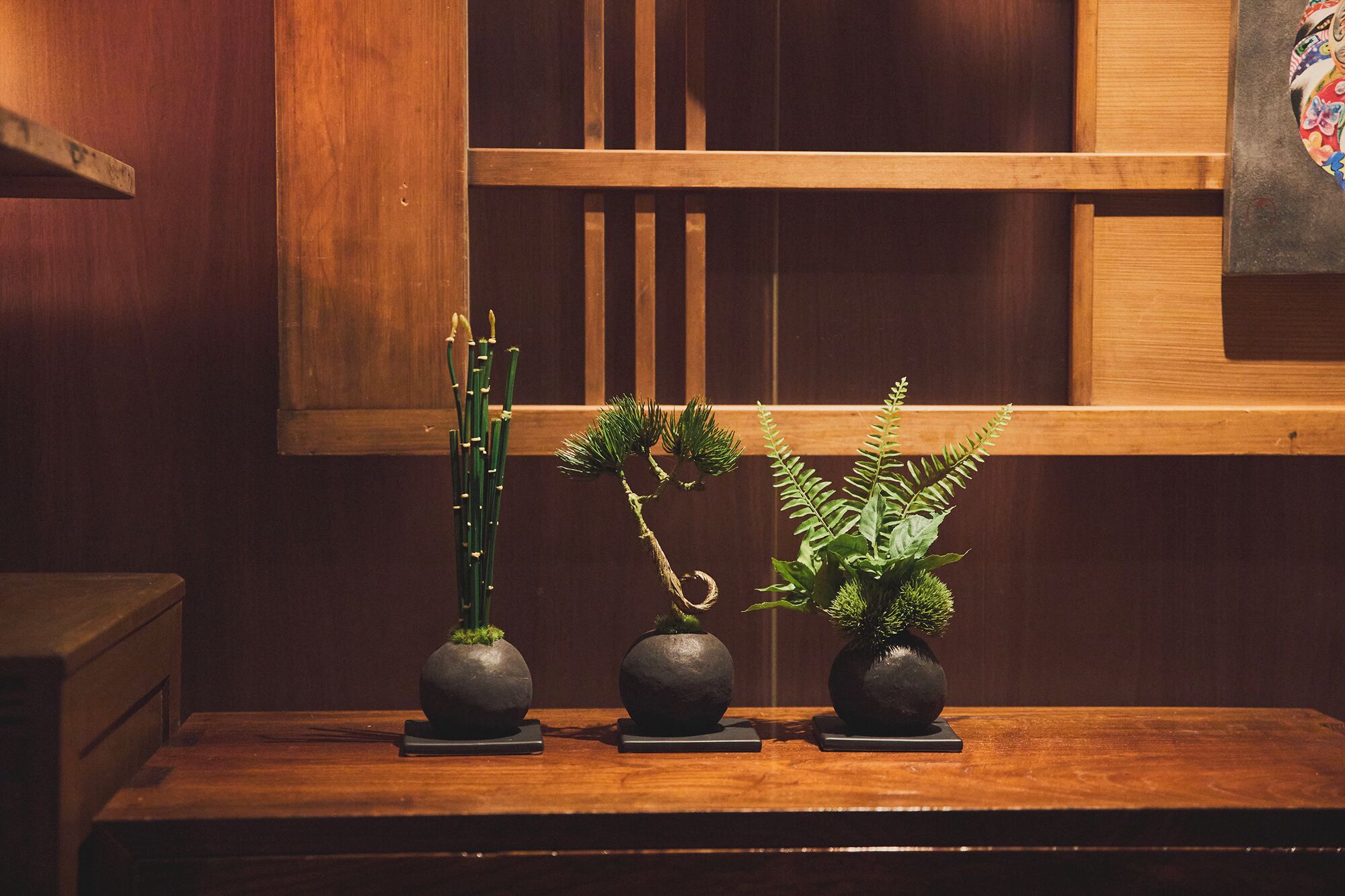 A wooden table with three dark spherical vases containing green plants.