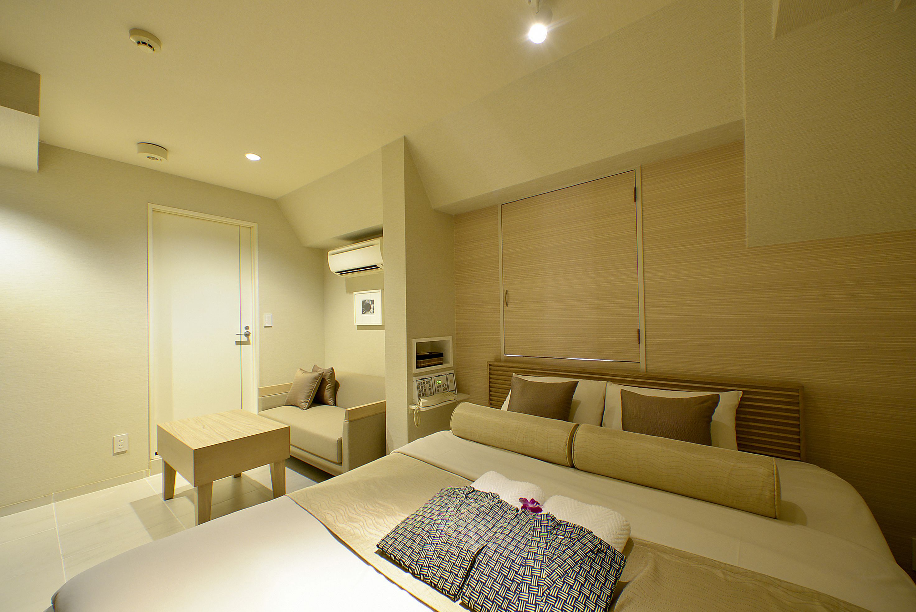 A modern hotel room with a large bed, bedside table, and a small desk.