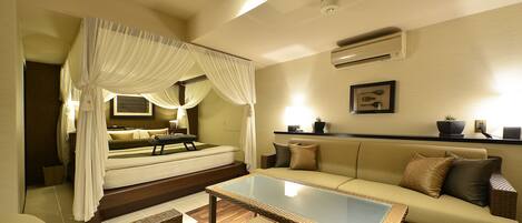 A bedroom with a canopy bed, a sofa, a glass-top coffee table, and a wall-mounted air conditioner.