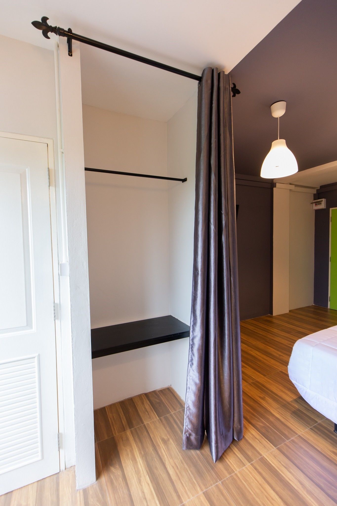 A bedroom with a bed, a hanging light fixture, a black shelf, and a door.