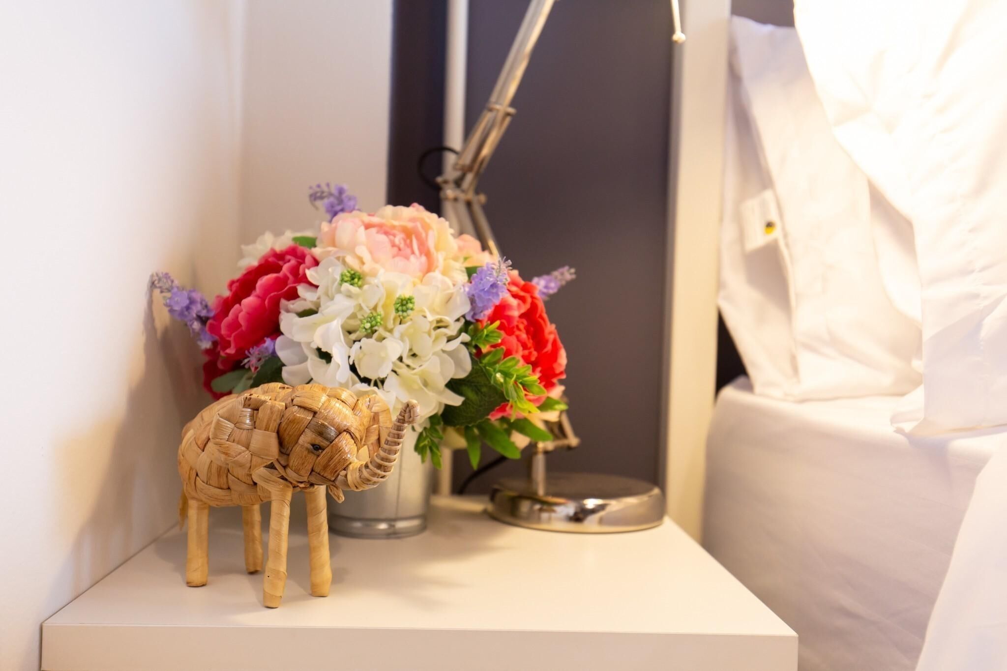 Una pequeña figurina de madera de elefante junto a un jarrón con flores sobre una mesita de noche.