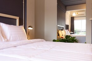 A neatly made bed with white linens, a bedside lamp, and a window with curtains. - Mango 10 House (Bangkok)