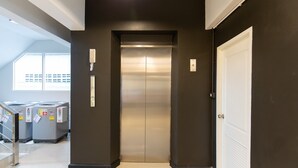 A modern elevator in a hallway with a dark wall and a white door on the right. - Mango 10 House (Bangkok)
