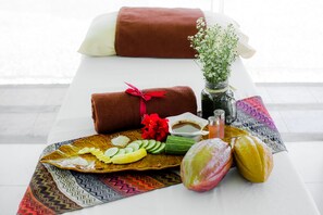 A spa setting with a massage table, towels, a tray of fruits, a vase with flowers, and a decorative pillow. - Malagos Garden Resort (Davao)