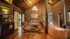 A log cabin interior with a wooden ceiling, a central seating area with a coffee table, and a fireplace. - Malagos Garden Resort (Davao)