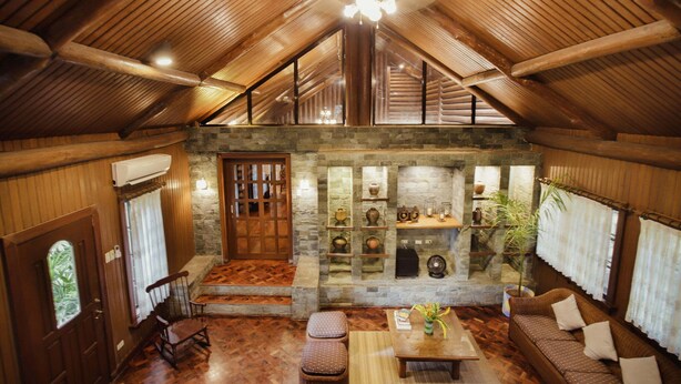 A cozy log cabin interior with a stone fireplace, wooden furniture, and a vaulted ceiling. - Malagos Garden Resort (Davao)