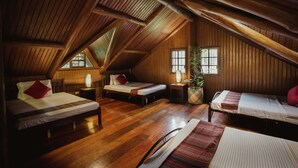 A cozy attic bedroom with wooden walls and sloped ceilings, featuring three beds and a large window. - Malagos Garden Resort (Davao)