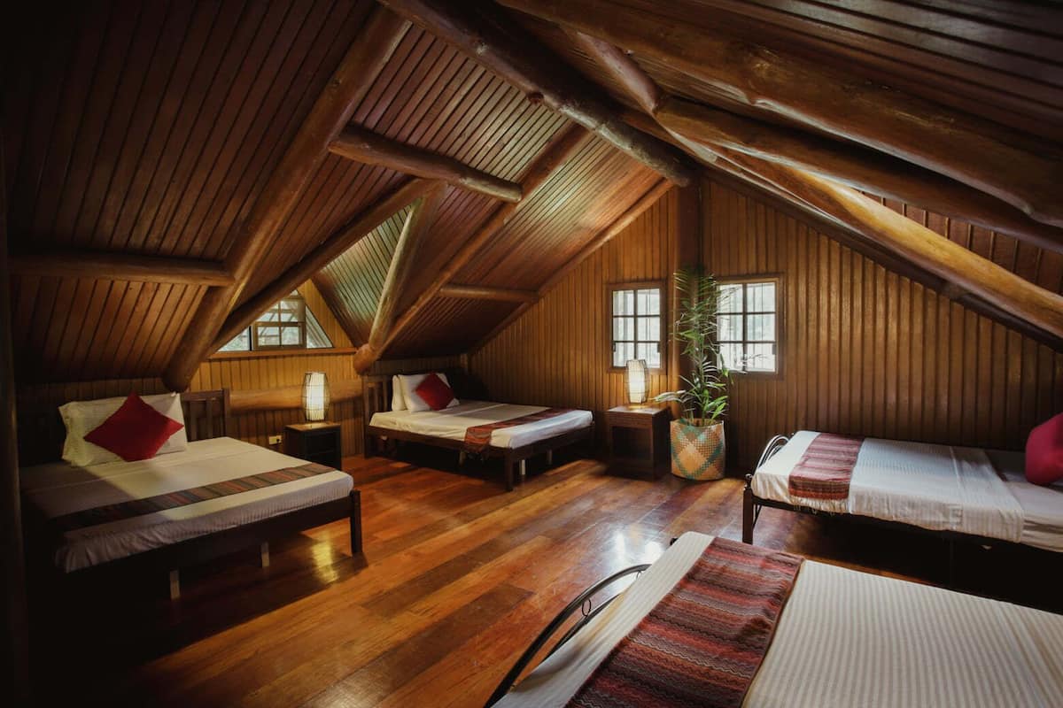Une chambre confortable située dans les combles, avec des murs en bois et un plafond en pente, comprenant trois lits et une grande fenêtre.