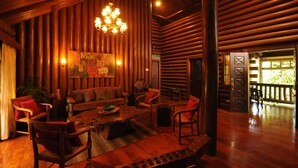 A log cabin interior with a wooden floor, a central seating area with a coffee table, and a chandelier. - Malagos Garden Resort (Davao)