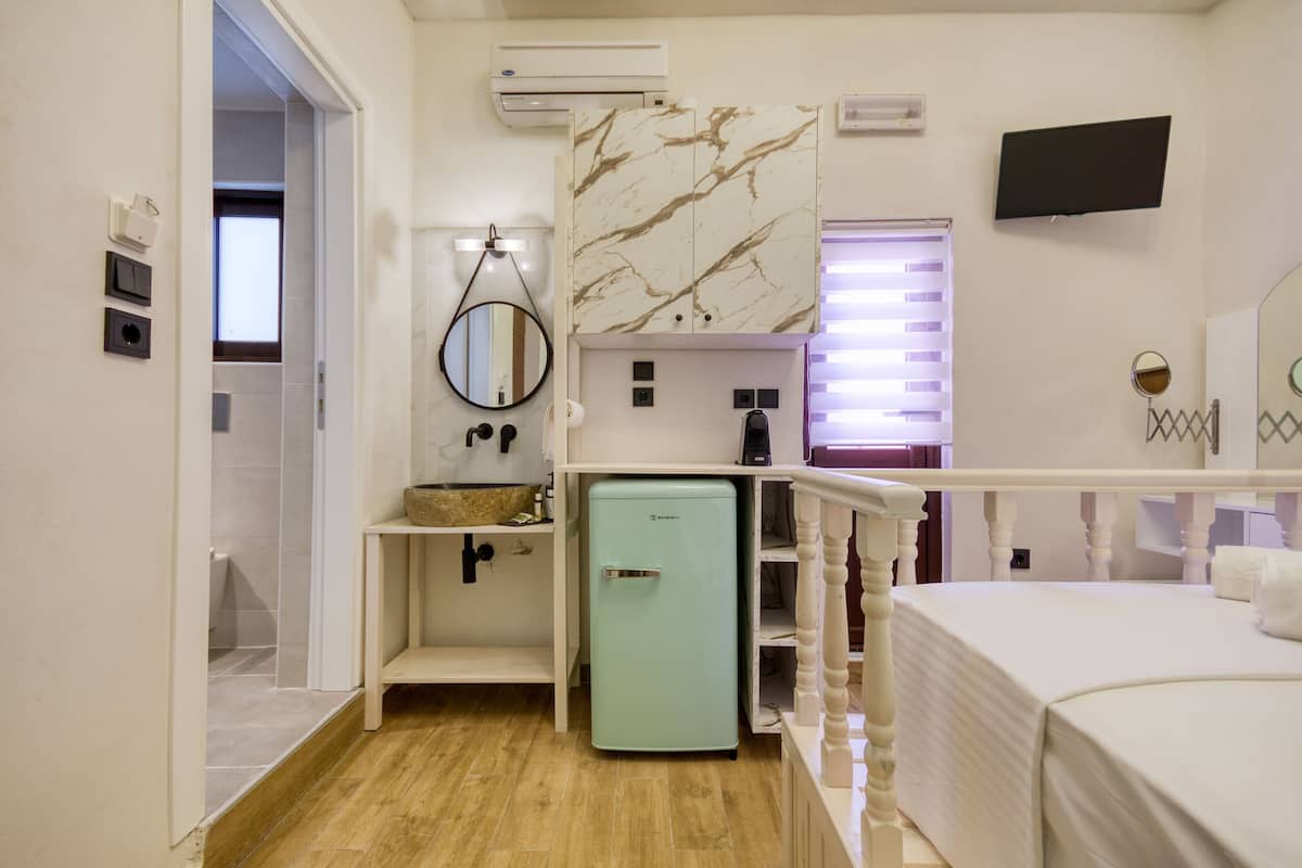 Een compacte hotelkamer met een houten vloer, een kleine kitchenette, een bed met wit beddengoed, een aan de muur bevestigde televisie en een kast met een marmerlook.