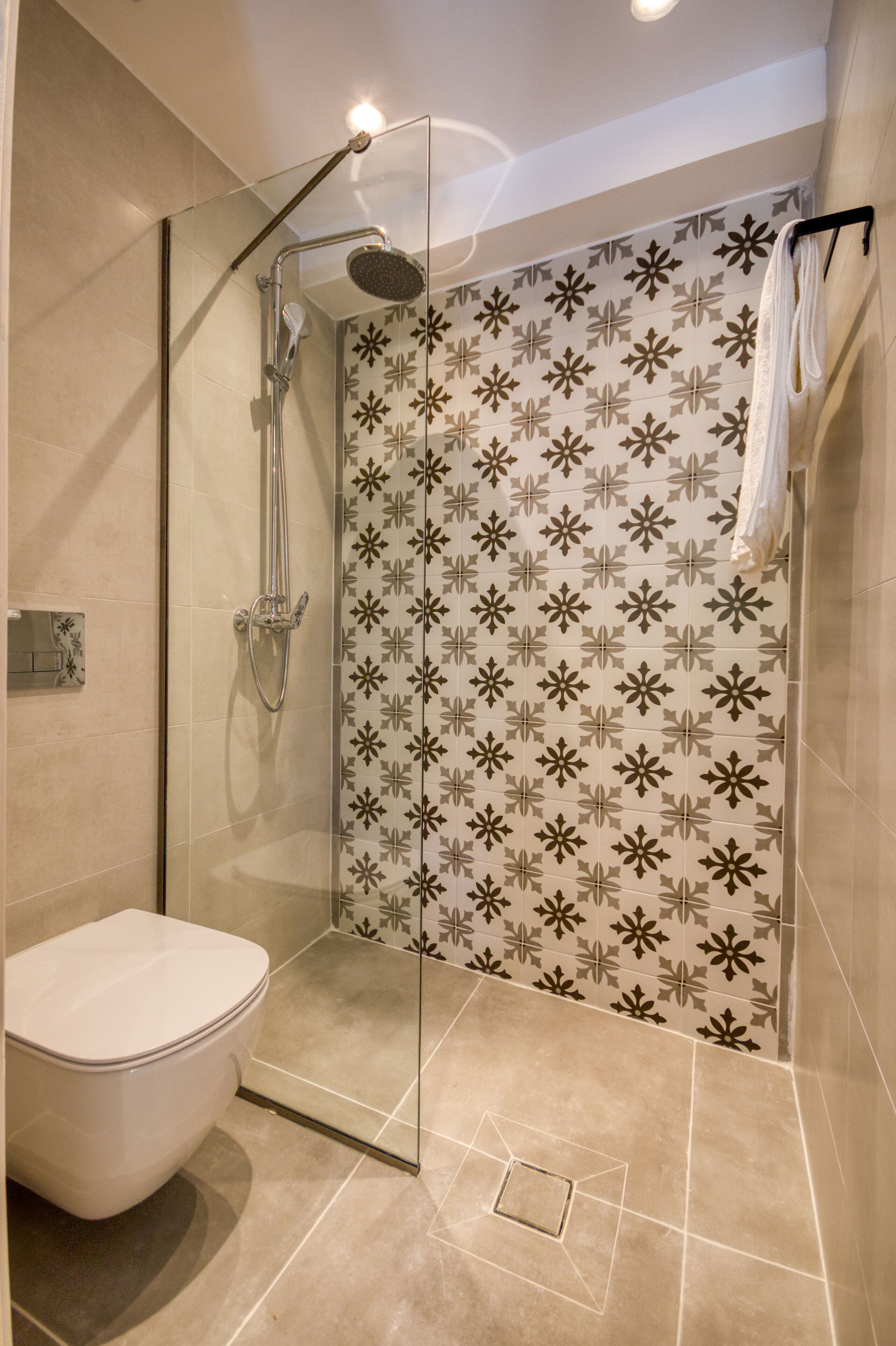 A modern bathroom with a glass-enclosed shower, a toilet, and patterned tiles.