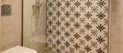 Un baño moderno con ducha envuelta en vidrio, un inodoro y baldosas estampadas.