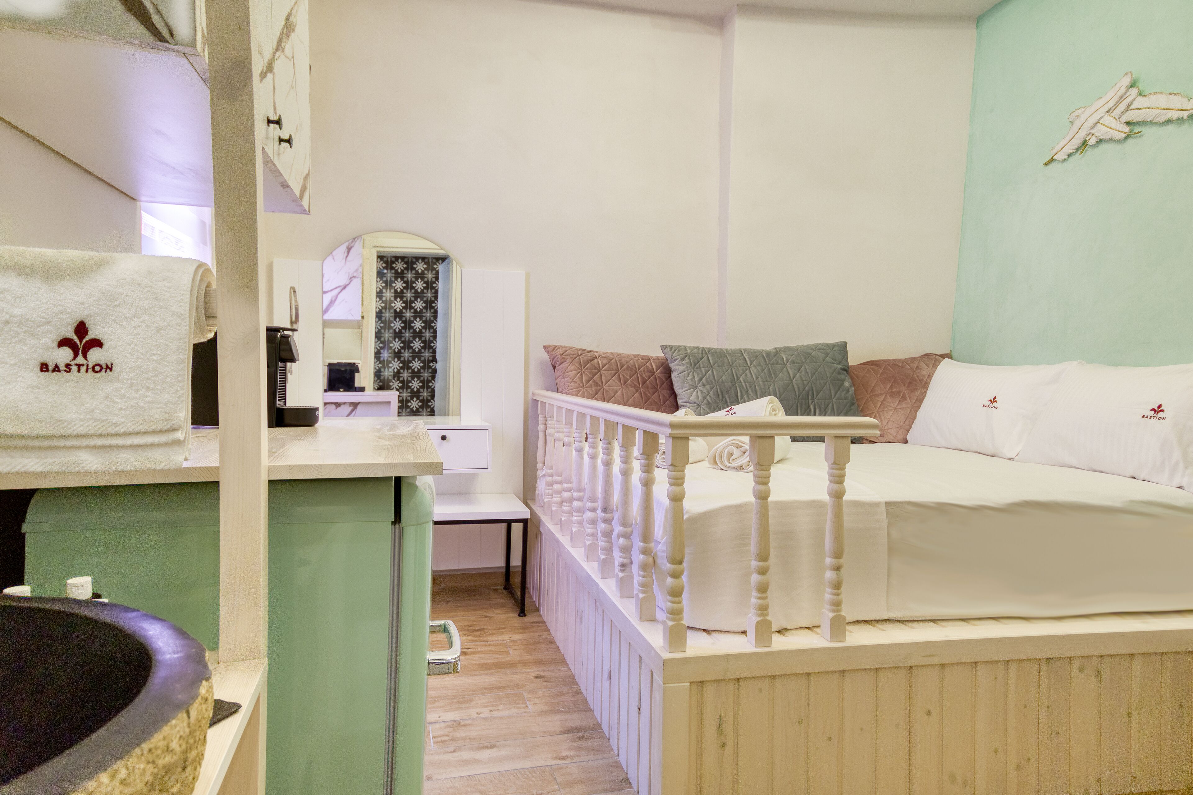 A bedroom with a bed, a small desk, a mirror, and a wall-mounted artwork.