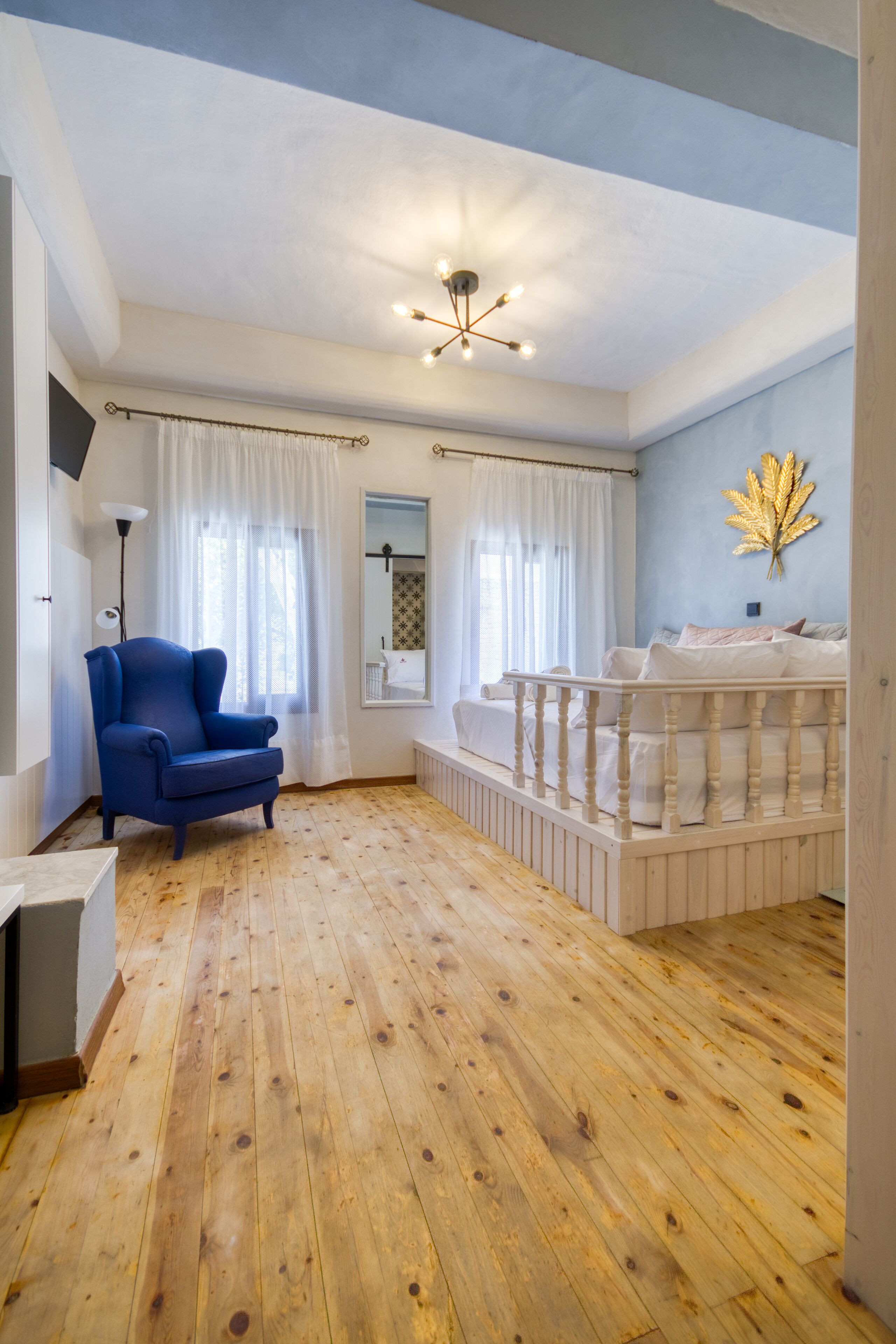 Une pièce avec un plancher en bois, un fauteuil bleu, un berceau blanc et un luminaire au plafond.