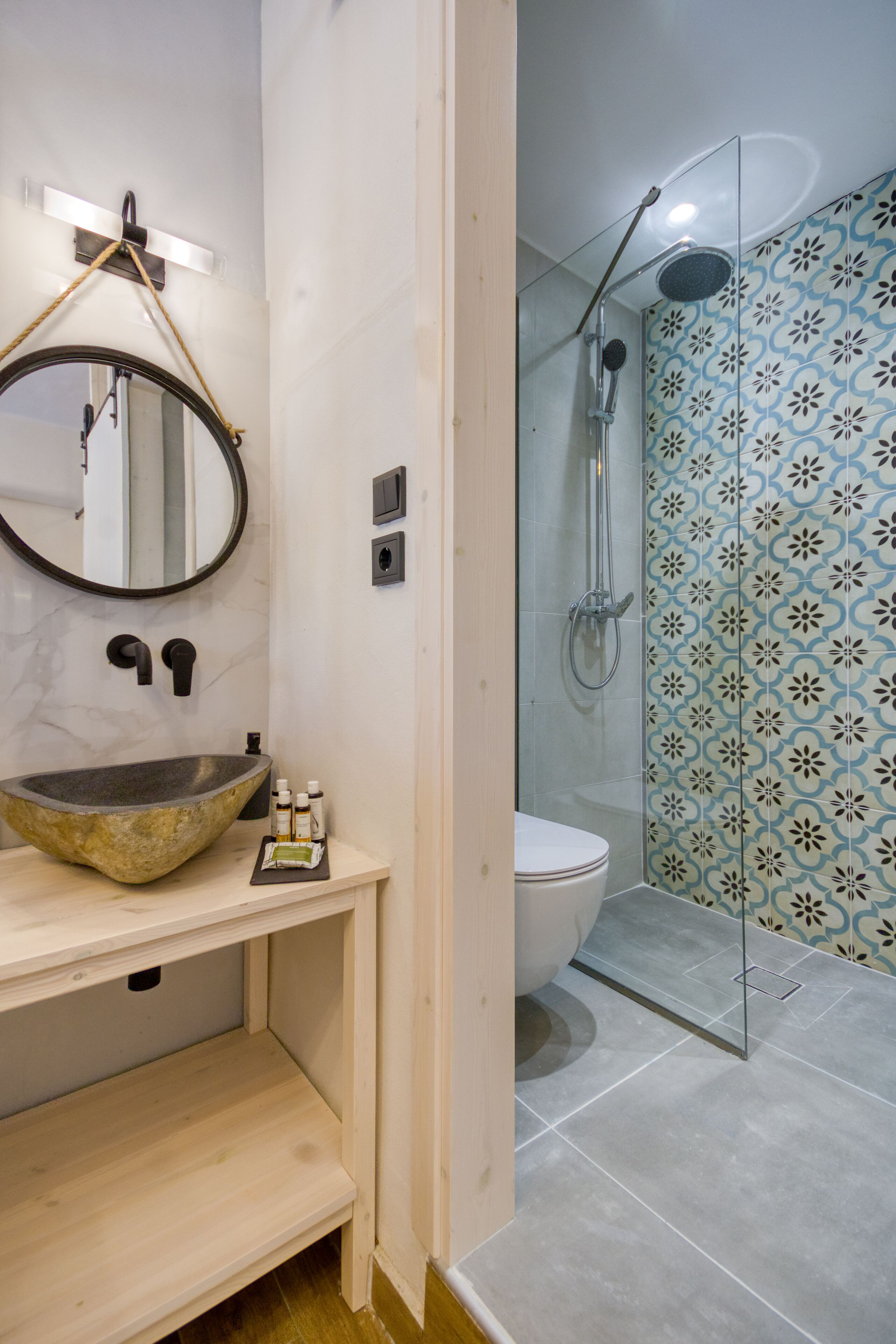 A bathroom with a stone sink, a mirror, a toilet, and a shower with patterned tiles.