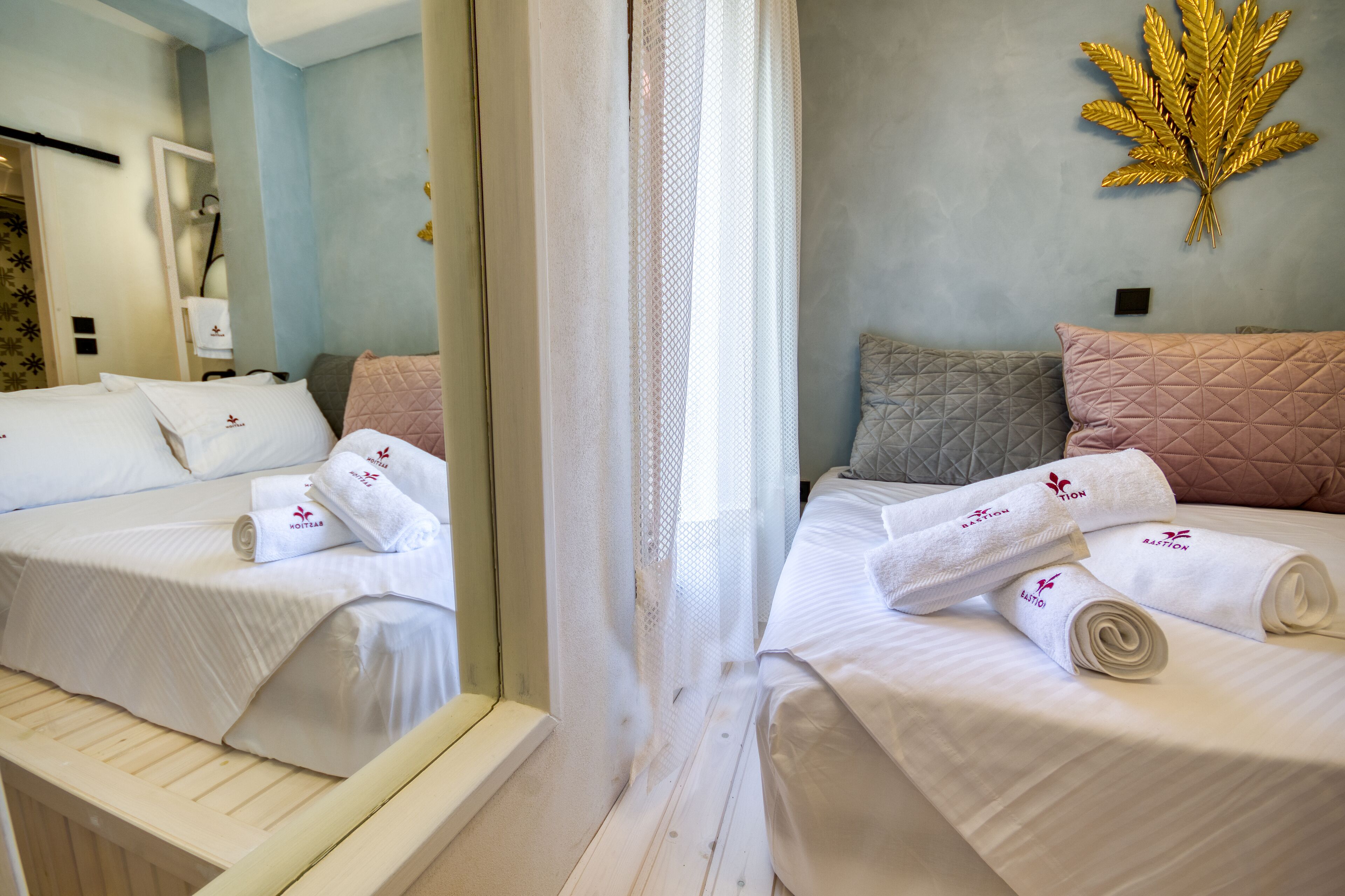 Habitación de hotel con dos camas, cada una con ropa de cama y toallas blancas, un espejo grande y una obra de arte decorativa con forma de hoja dorada en la pared.