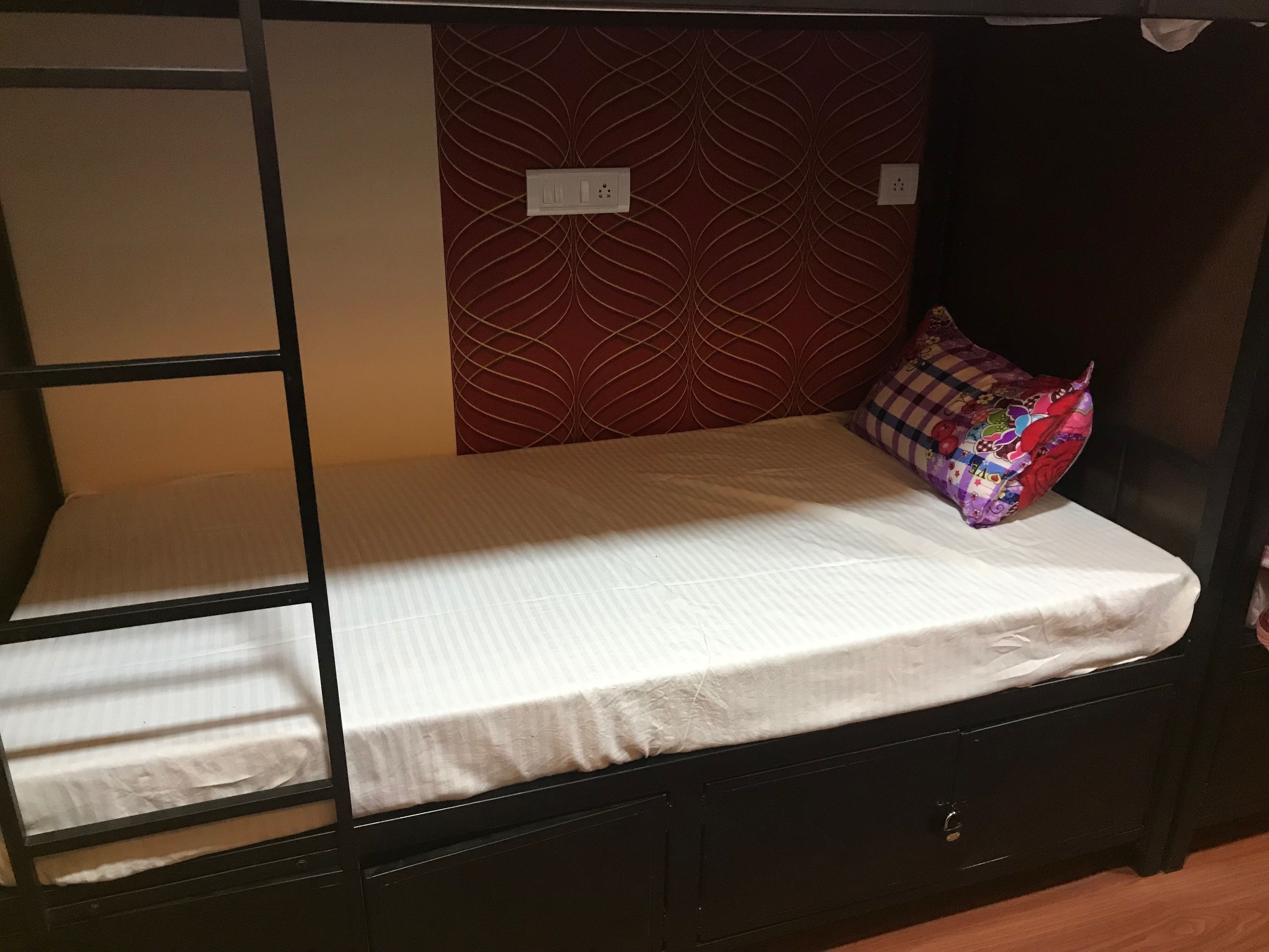 Un letto a castello con materasso e cuscini, una parete con motivo geometrico e una presa di corrente.
