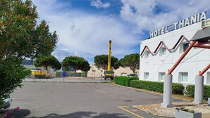 A hotel named "HOTEL THANIA" with a parking lot and a yellow crane in the background. - Hotel Thania (Frontignan)