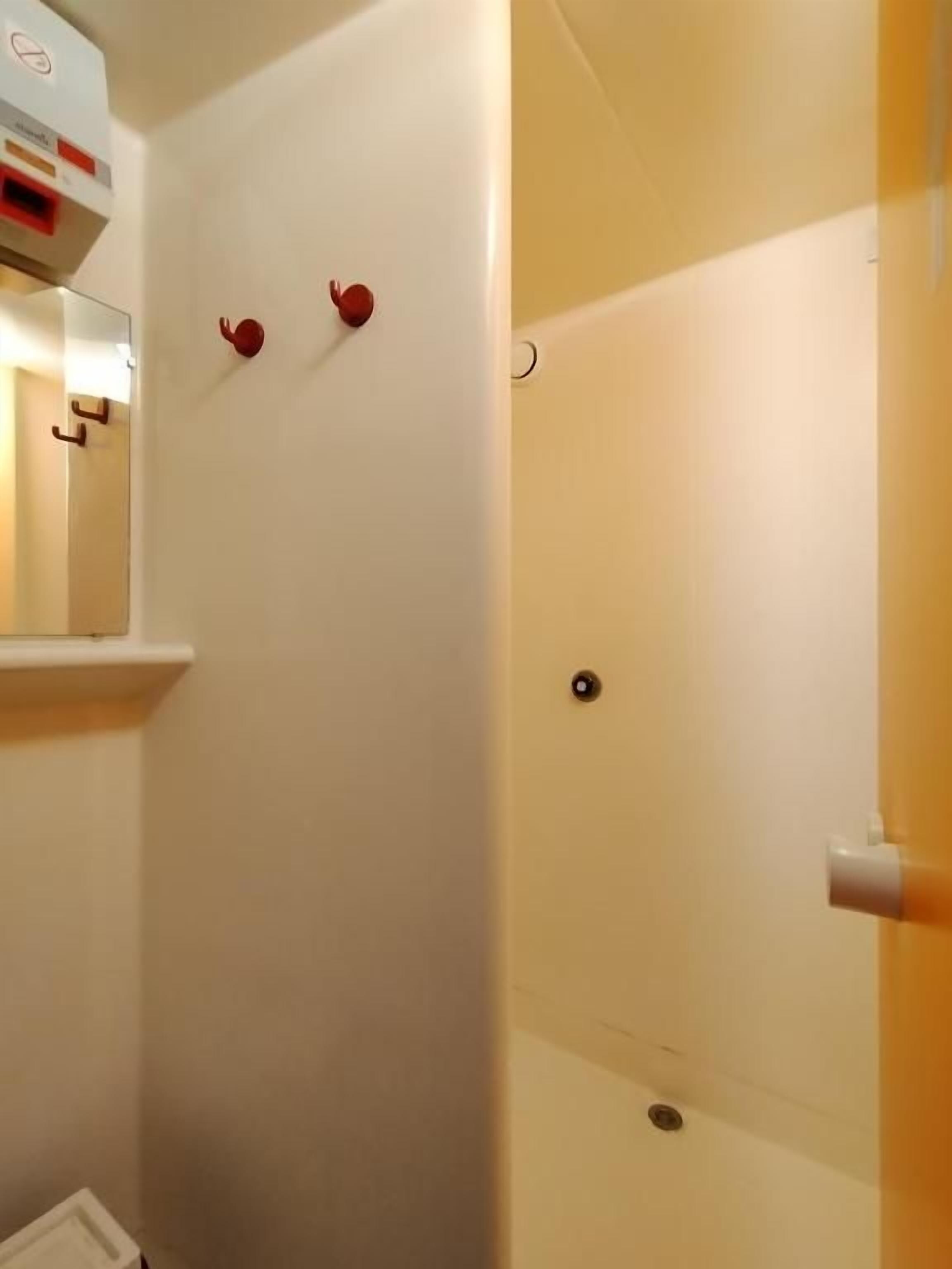 A bathroom with a white wall, a mirror, and a shower area.