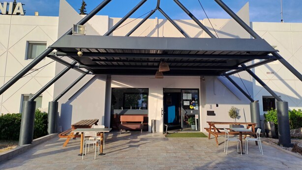 A modern building with a triangular roof structure, outdoor seating area with tables and chairs, and a visible entrance. - Hotel Thania (Frontignan)