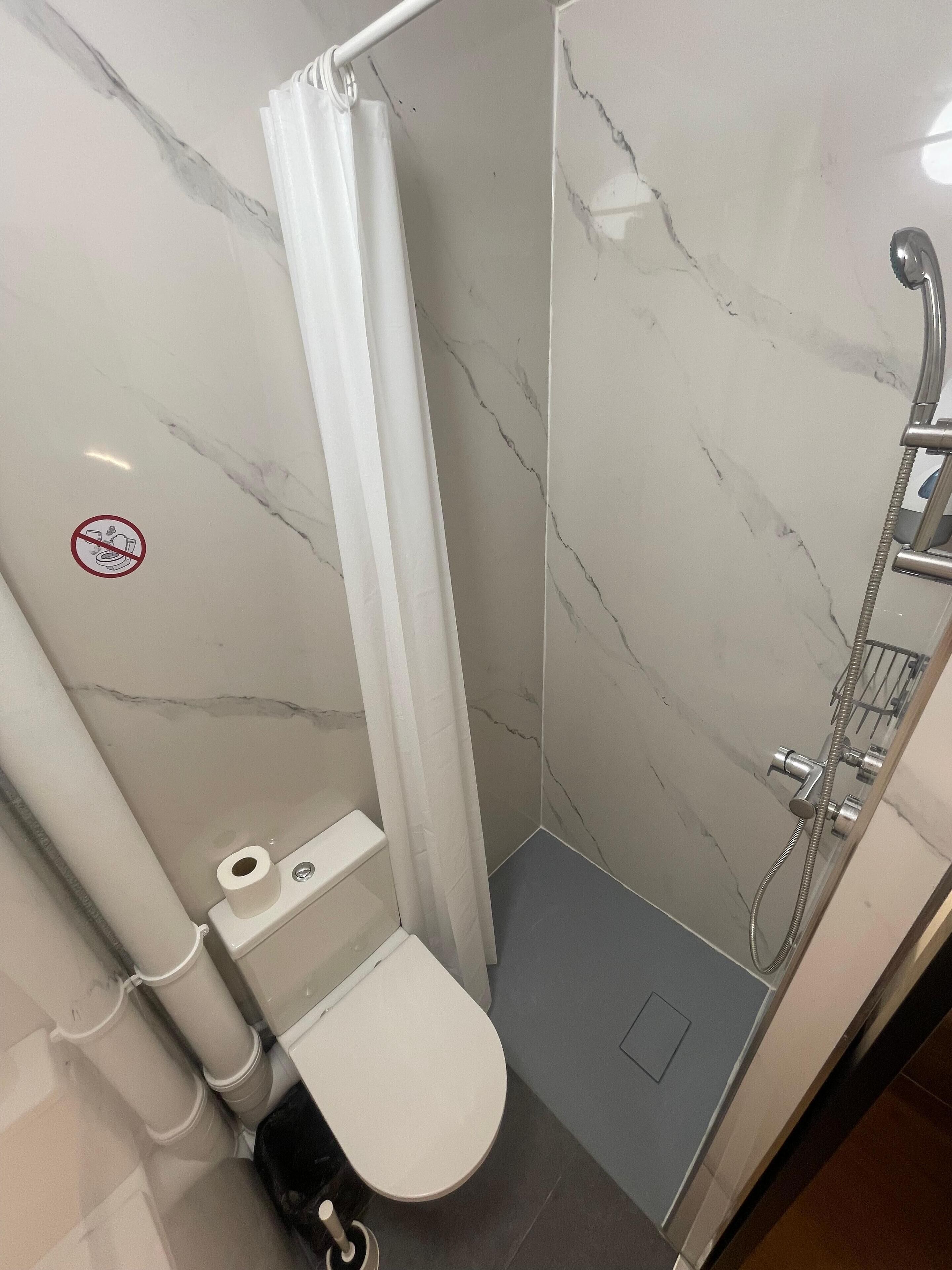A small, modern bathroom with a shower, toilet, and a no-smoking sign on the wall.