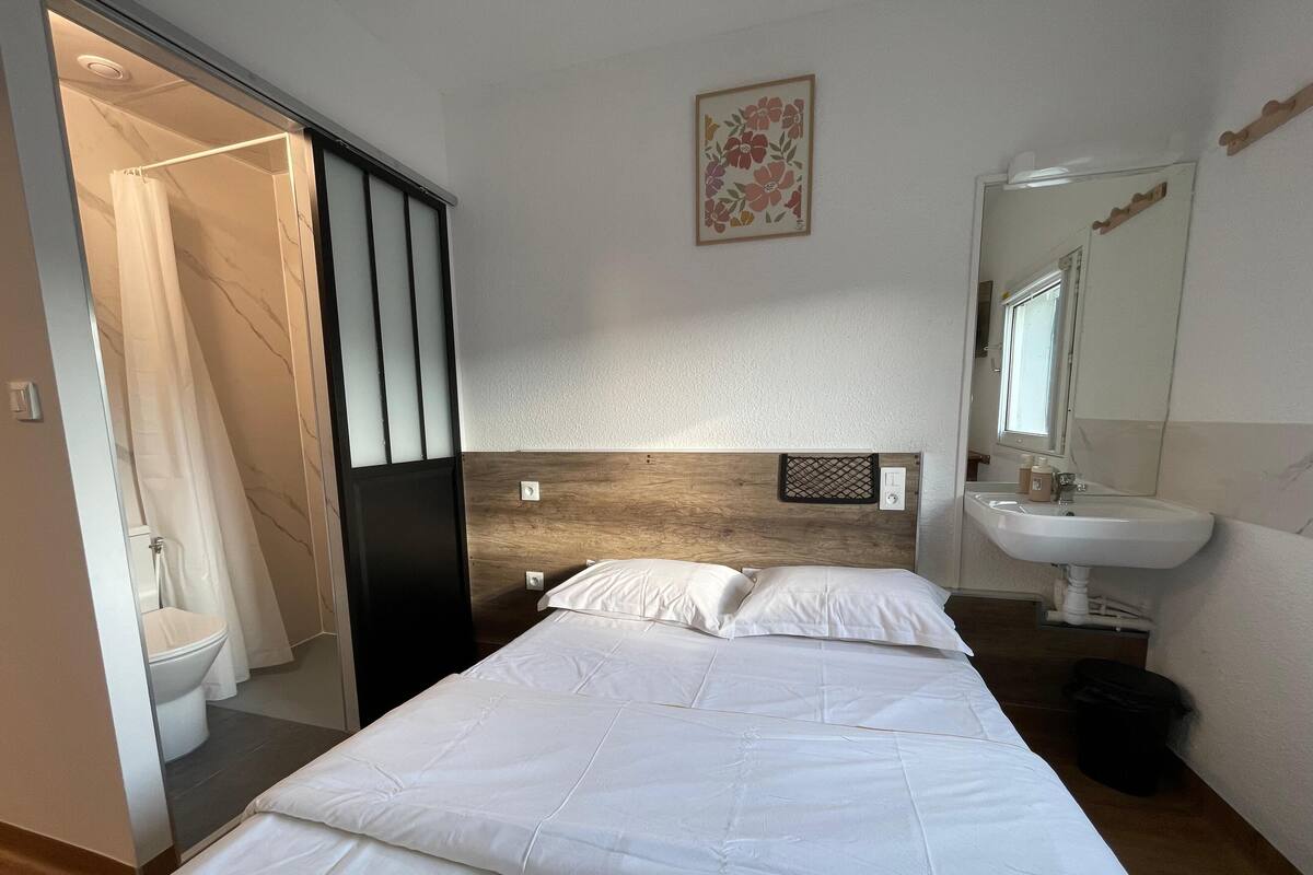 Une chambre d’hôtel avec un lit, une tête de lit en bois, une salle de bain avec un lavabo et une douche.