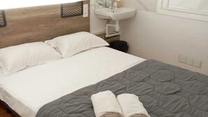 A hotel room with a bed, a grey quilted bedspread, two rolled towels, a white sink, and a mirror above it. - Hotel Thania (Frontignan)