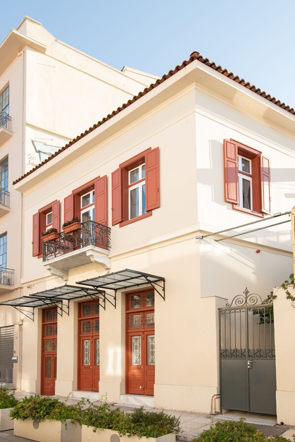 A two-story building with red shutters, a balcony with wrought iron railings, and a gated entrance. - Ether Loft Suites (Athens)