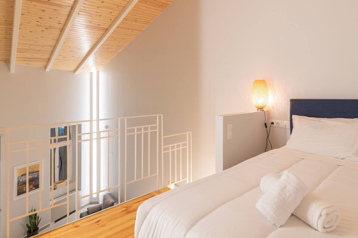 Un dormitorio con cama, lámpara de noche, ventana y vistas a un balcón.