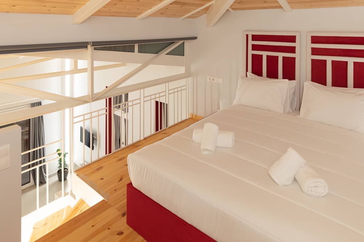 Un dormitorio con techo de madera, una cama con ropa de cama blanca y vistas al exterior.