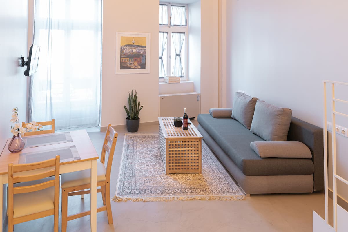 Amplia sala de estar con techo de madera, un sofá gris, una mesa de comedor con sillas, una mesita de centro y una planta en maceta.