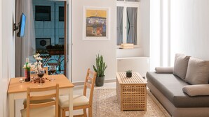 Una sala de estar con techo de madera, un sofá gris, una mesa de comedor con sillas, una pequeña planta en maceta y un cuadro en la pared.