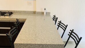 A kitchen with a granite countertop, a gas stove, and four black chairs.