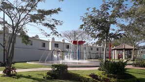 A courtyard with a fountain, surrounded by greenery and a building with a tiled roof.
