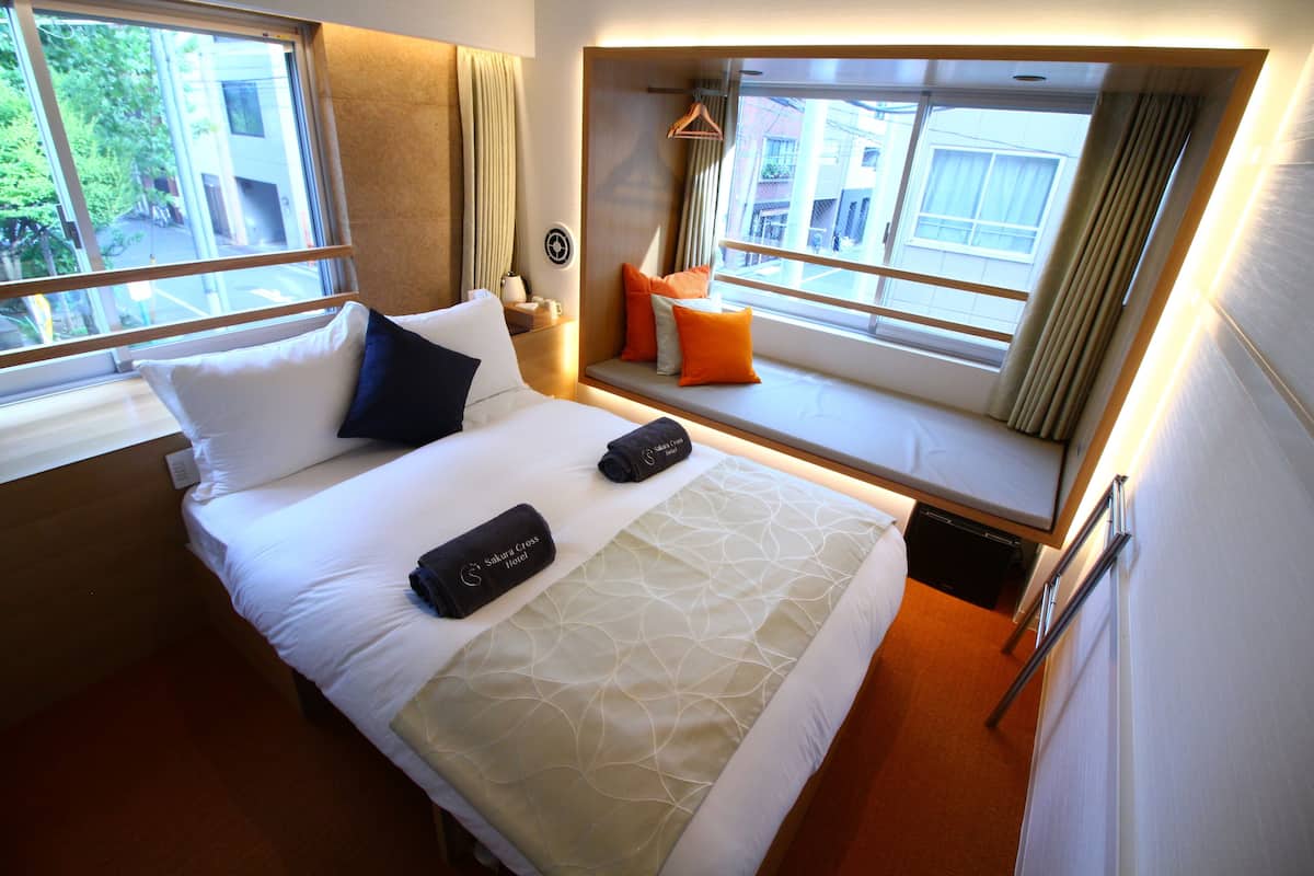 Een hotelkamer met een bed, kussens, een vensterbank en uitzicht.