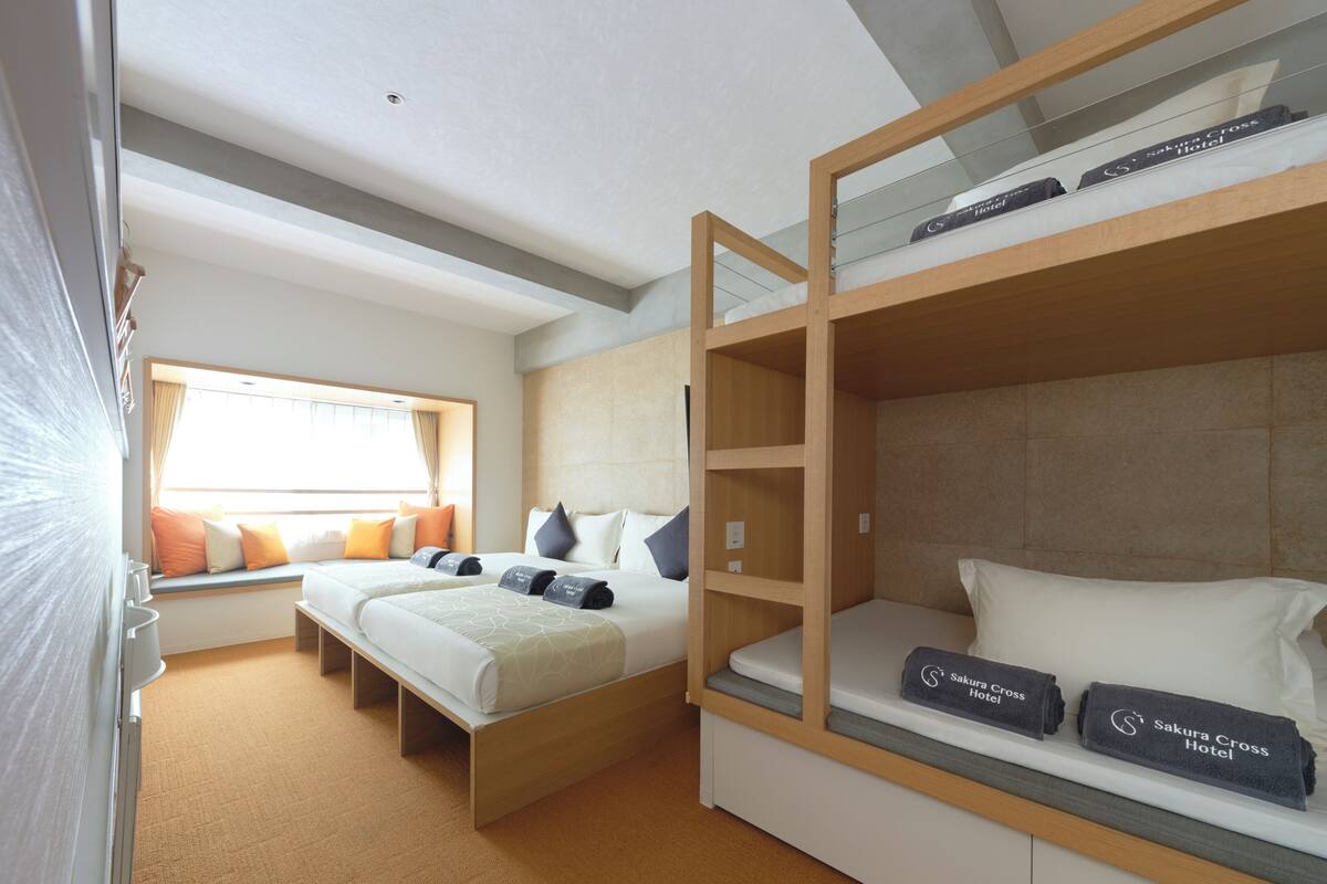 Een hotelkamer met een stapelbed, een eenpersoonsbed, een raam met gordijnen en uitzicht op de omgeving.