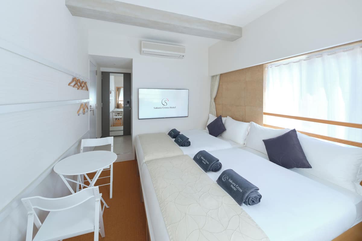 Een hotelkamer met een bed, een bureau en een stoel. Er is een televisie aan de muur en een raam met gordijnen.