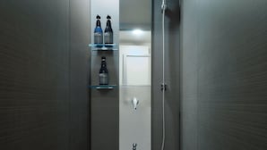 Un baño moderno con cabina de ducha de vidrio, inodoro empotrado y estante con artículos de aseo.