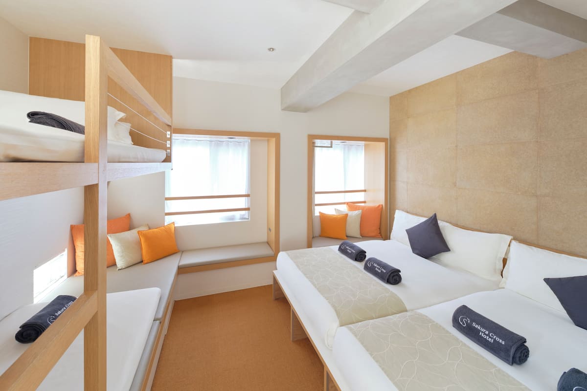 Een hotelkamer met stapelbedden, een groot bed en een raam met gordijnen.