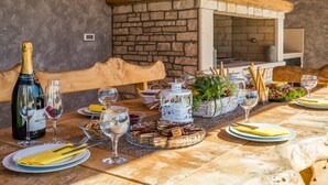An outdoor dining area with a stone wall, wooden furniture, and a variety of food and drink items. - Villa Mabuhay (Marcana)