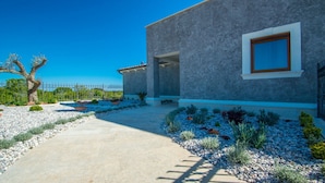 A modern house with a stone facade, a concrete driveway, and a garden with various plants and a tree. - Villa Mabuhay (Marcana)