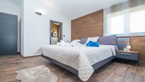 A modern hotel room with a large bed, a nightstand, a wooden headboard, and a large window with curtains. - Villa Mabuhay (Marcana)