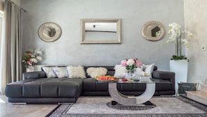 A modern living room with a dark leather sectional sofa, a glass coffee table, and decorative mirrors on the walls. - Villa Mabuhay (Marcana)