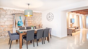 A modern dining area with a stone wall, a round wall clock, and a dining table with chairs. - Villa Lucia (Marcana)