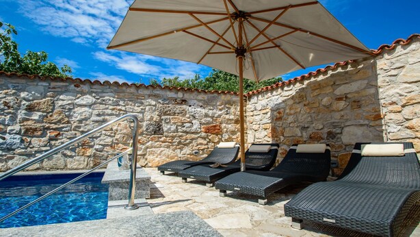 A stone-walled outdoor pool area with lounge chairs and an umbrella. - Villa Lucia (Marcana)