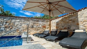 A stone-walled outdoor pool area with lounge chairs and an umbrella.